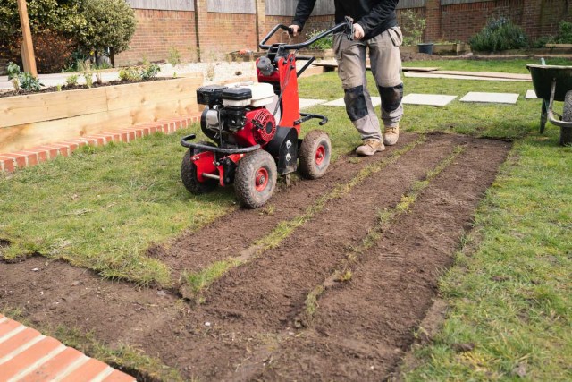 A gardener pushes a motorized sod cutter.