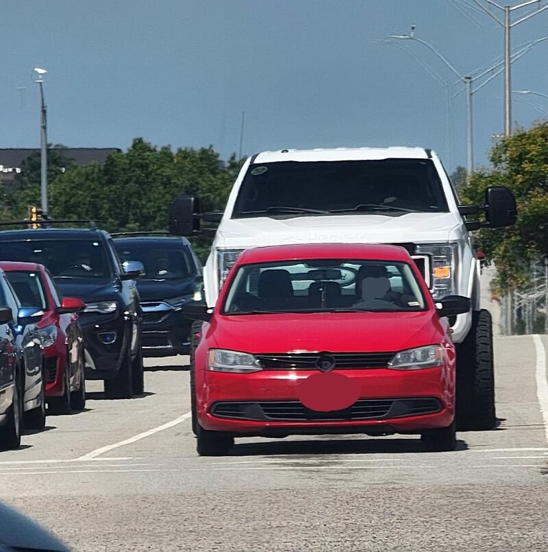 The dramatic height difference between the modified truck and standard cars poses significant risks in the event of a collision.