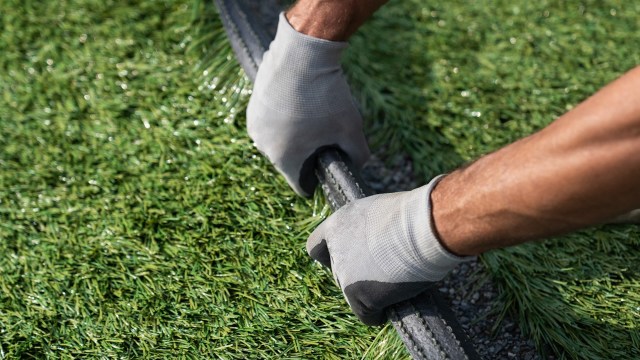 Gardener with gloves on touching artificial turf.